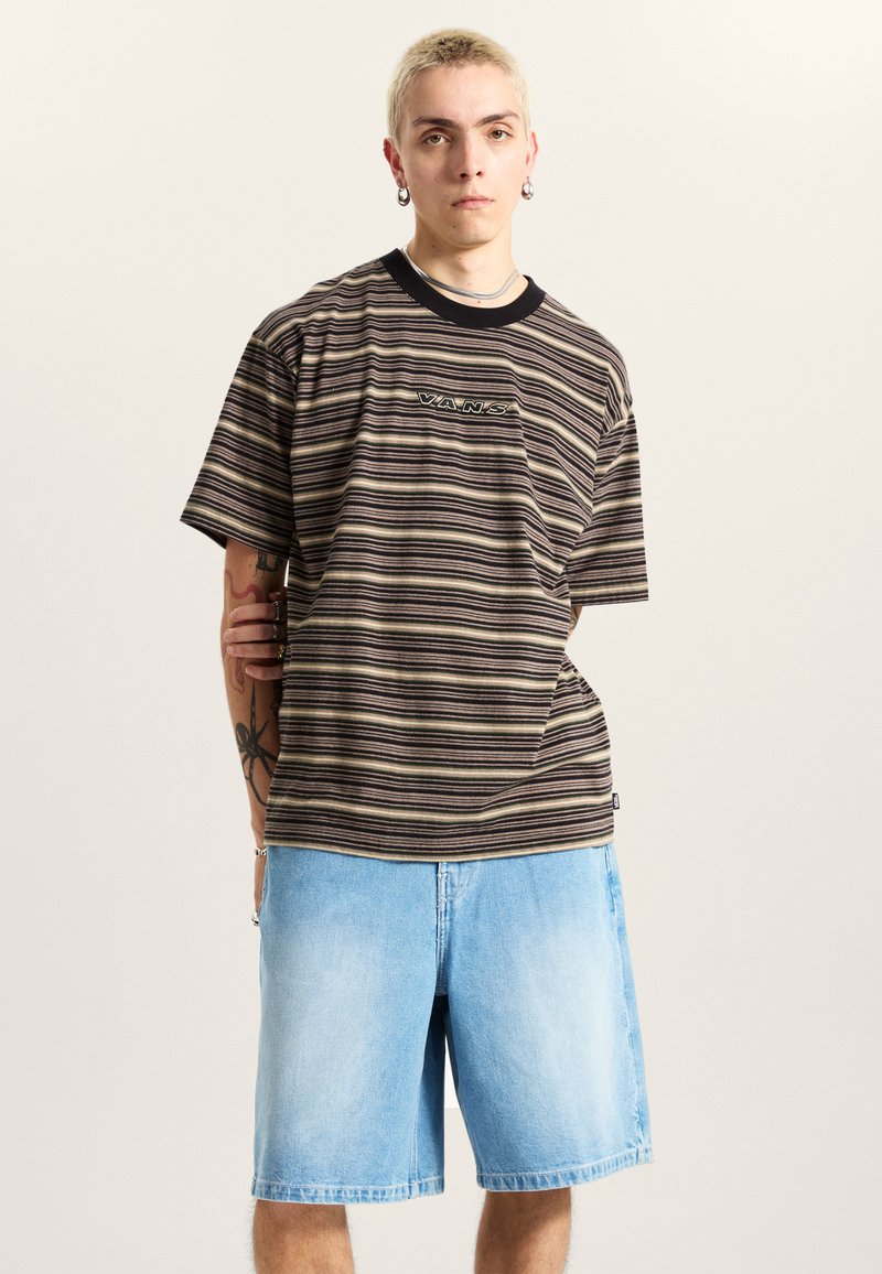 Camiseta de manga corta a rayas en tonos marrones y crema con ribete y logo negros. Combinada con pantalones cortos de mezclilla azul claro. Textura suave.
