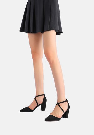 Scarpe con tacco alto in suede nero, a punta e con tacco a blocco. Presentano cinturini incrociati alla caviglia e una texture liscia.