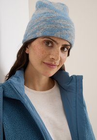 Beanie a righe blu e grigie, texture morbida. Il modello indossa una giacca in pile blu sopra una maglietta chiara, con uno sfondo neutro.
