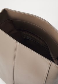Beige nahkainen laukku, jossa on sileä pinta, jossa on vetoketjullinen tasku sisällä ja näkyvät saumat ulkopuolella.