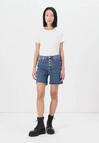 Jeanshorts med høy midje, fem-knappsgylf og frontlommer, sammen med en tettsittende hvit t-skjorte og svarte lisse-up kampstøvler.
