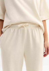 Beige oversized t-shirt gecombineerd met bijpassende zachte, elastische broek met tailleband en zijzakken. Gladde, gestructureerde stof.