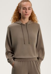 Beżowa bluza z kapturem o luźnym fasonie, wyposażona w sznurek do regulacji kaptura, ściągacze na rękawach oraz miękką teksturę, w zestawie z pasującymi spodniami.