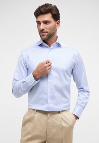 Camicetta azzurro chiaro con sottili righe bianche, colletto a bottoni, e maniche lunghe, con bottoni bianchi e una texture di cotone liscia.