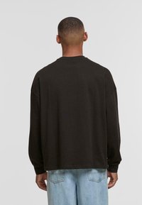 Dark brown long-sleeve shirt with a relaxed fit and drop shoulders, paired with light blue denim jeans, showing a simple design.