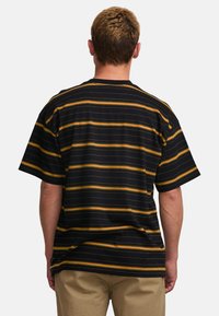 Camiseta negra a rayas con líneas horizontales amarillas y naranjas, corte holgado, mangas cortas y cuello de canalé. Textura de tejido suave.