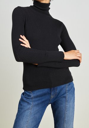 Pull à col roulé noir à côtes avec des manches longues, présentant une coupe ajustée et un motif texturé, assorti à un jean en denim bleu.