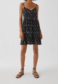 Robe noire à fleurs avec un ourlet évasé, des bretelles spaghetti réglables et une délicate bordure en dentelle. Présente de petits motifs de fleurs blanches et violettes.