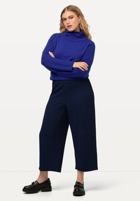 Suéter azul de punto con cuello alto, combinado con pantalones anchos de patrones en azul marino y zapatos negros de suela gruesa. Presenta textura acanalada y un corte relajado.