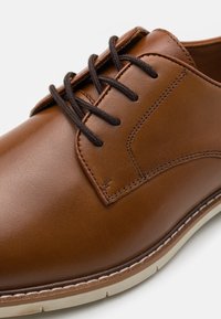 Scarpa in pelle marrone con lacci, dalla finitura liscia, punta rotonda, cuciture a contrasto e suola in gomma di colore chiaro.