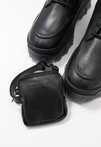 Czarne skórzane buty z teksturowaną podeszwą oraz pasującą czarną skórzaną torebką. Buty mają wyraźne szwy i regulowane sznurówki.