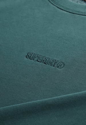 Bluza w kolorze morskim z prążkowanym kołnierzem, ozdobiona wytłoczonym logo „SUPERDRY”. Wykonana z miękkiego materiału, o gładkiej fakturze i solidnym szyciu.