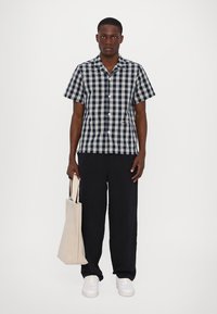 Ναυτικό και κρεμ καρό πουκάμισο κοντό μανίκι, μαύρο παντελόνι wide-leg, λευκά αθλητικά παπούτσια και μπεζ τσάντα ώμου. Απλά κουμπιά και λεπτομέρειες σχέδιο.