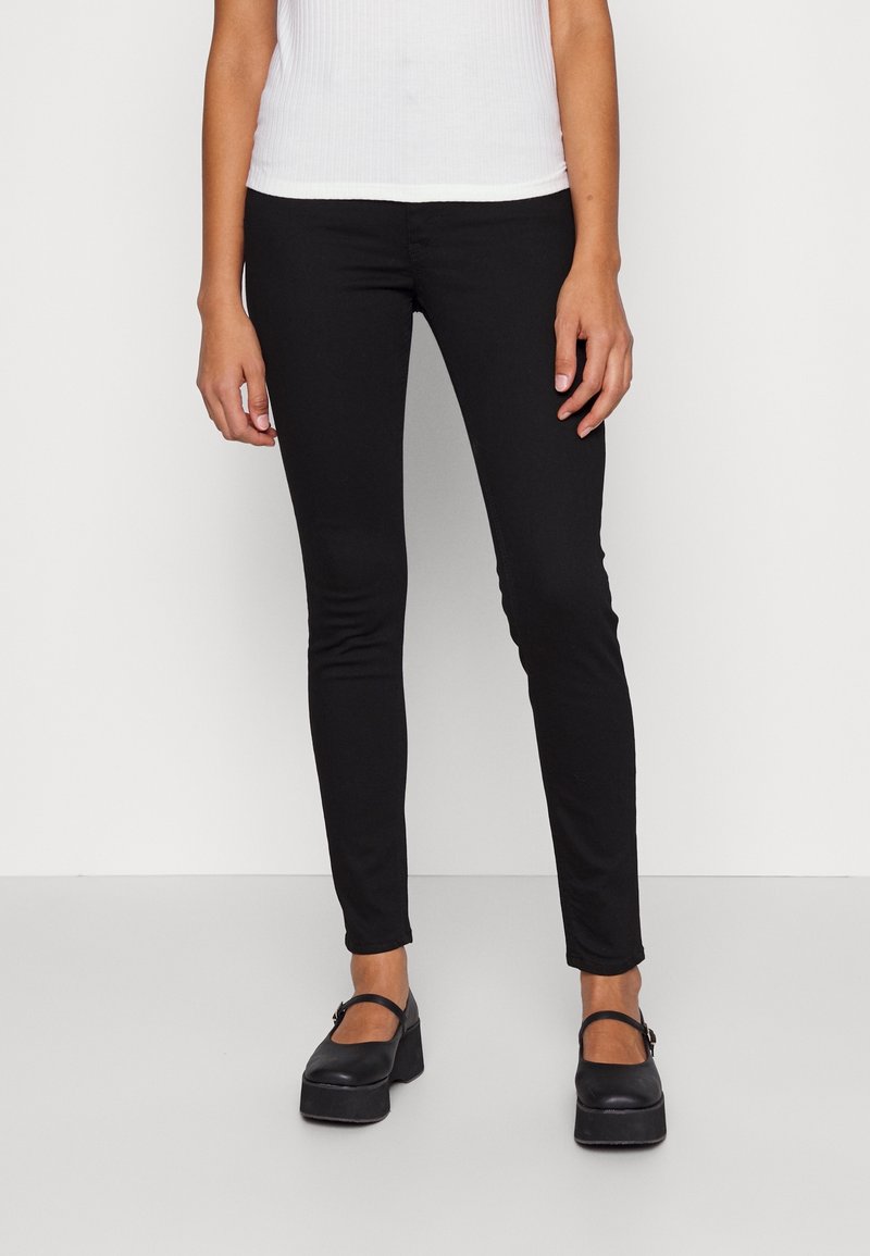 Jeans neri skinny realizzati in tessuto elastico, con un design aderente e vita media. Abbinati a scarpe con plateau nere.