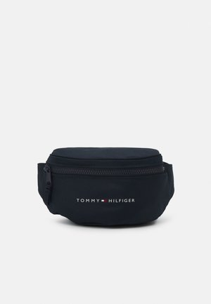 Sacoche de taille bleu marine avec une fermeture éclair en haut, présentant une texture lisse et un logo de marque imprimé en blanc et rouge sur le devant.