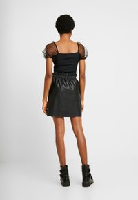 Czarna bluzka z bufiastymi rękawami z przezroczystego materiału w kropki, zestawiona z mini spódnicą z wysokim stanem z ekoskóry. Czarne botki za kostkę z klamrami.