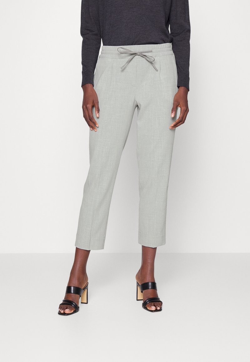 Personne portant un pantalon court gris clair avec taille à cordon, un haut noir à manches longues et des sandales à talons noires à bout ouvert.