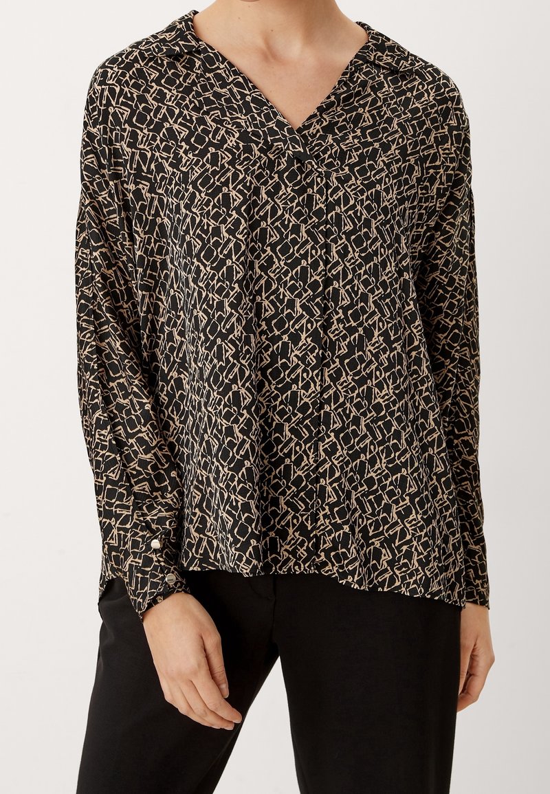 Blouse noire et beige à motifs avec un col en V, des manches longues et des poignets boutonnés ; fabriquée en tissu léger avec une coupe ample.