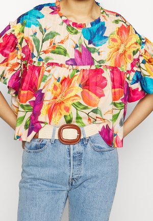 Floral blouse with ruffled sleeves, featuring multicolored lilies and leaves on a light background, paired with light blue jeans and a beige belt.