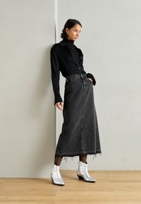 Camisa negra de botones con mangas largas, combinada con una falda maxi de mezclilla gris con dobladillo deshilachado y botas de tobillo plateadas.