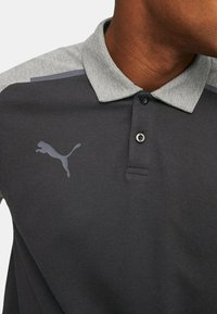 Polo grigio scuro con colletto grigio chiaro, caratterizzato da un logo Puma discreto. Tessuto testurizzato e dettagli con abbottonatura a due bottoni.