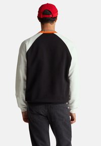 Czarna bluza z białymi raglanowymi rękawami. Posiada zaokrąglony dekolt, luźny krój oraz ściągacze przy mankietach. Połączona z ciemnymi dżinsami.