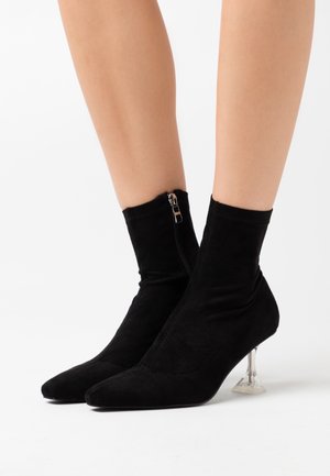 Botas negras hasta el tobillo de material suave similar a ante, con cierre de cremallera y un tacón transparente con forma geométrica.