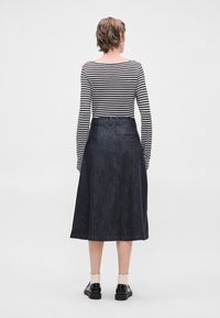 Τζιν φούστα με φουσκωτό σχέδιο, σκούρο μπλε χρώμα, λεπτομέρεια πίσω τσέπης και ζώνη. Συνδυασμένη με ριγέ μπλούζα μακρυμάνικη και μαύρα παπούτσια.