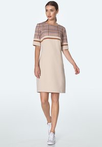 Beżowa sukienka z geometrycznym, kraciastym gorsetem, krótkimi rękawami i kontrastowymi paskami. Z połączeniem białych sneakersów, gładka tekstura materiału.
