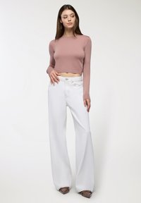 Różowy, krótki sweter z długim rękawem, połączony z białymi spodniami o szerokich nogawkach, z klasycznym zapięciem na guziki i subtelnymi detalami ściegów.