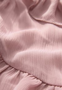 Strukturiertest pinkes Gewebe mit vertikalen Rippungen und weichem Fall; verfügt über geraffte Details am Saum für zusätzliche Dimension.