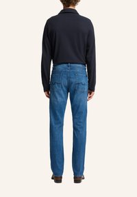 Polo a maniche lunghe blu della marina abbinato a jeans in denim blu. I jeans presentano due tasche posteriori con cuciture decorative. Scarpe marroni visibili.