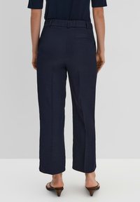 Pantalons amples bleu marine avec une texture lisse, taille relaxée et détail de poche arrière, associés à des sandales à talons bruns.