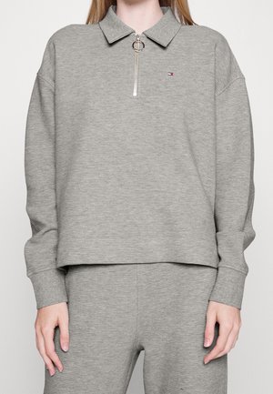 Haut gris côtelé à manches longues avec col et fermeture éclair partielle, associé à un pantalon côtelé assorti, porté par une personne du cou jusqu'aux cuisses.