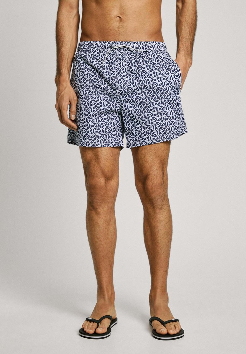 Costumi da bagno da uomo in blu navy con un motivo astratto bianco. Realizzati in tessuto leggero, presentano una vita elasticizzata e tasche laterali.