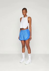 Valge lühike top, sinised sportlikud lühikesed püksid mustade aktsentidega, valged spordijalatsid ja valged sokid, millel on must logo.