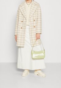 Beige hundtandsmönstrad kappa med stora slag, vit ribbad topp, vit denimkjol, grön krokodilprägling väska och beige klumpiga stövlar.