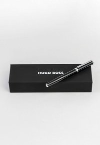Stylo noir Hugo Boss reposant sur une boîte noire ; le stylo présente un corps élégant avec des accents chromés, une finition lisse et une pointe arrondie.