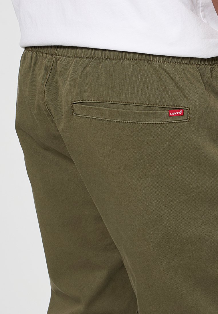 Primo piano della tasca posteriore dei pantaloni Levi's verde oliva con etichetta rossa Levi's, indossati con una camicia bianca infilata dentro.