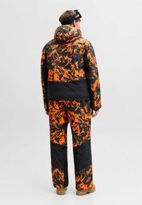 Chaqueta y pantalones de invierno aislados de color negro con patrones naranjas. Cuenta con una capucha, un diseño abstracto audaz y un ajuste relajado para mayor comodidad.