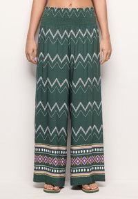 Green wide-leg pants with a smocked waistband. Features white zigzag and patterned hem with purple, yellow, and red accents. Lightweight fabric.
