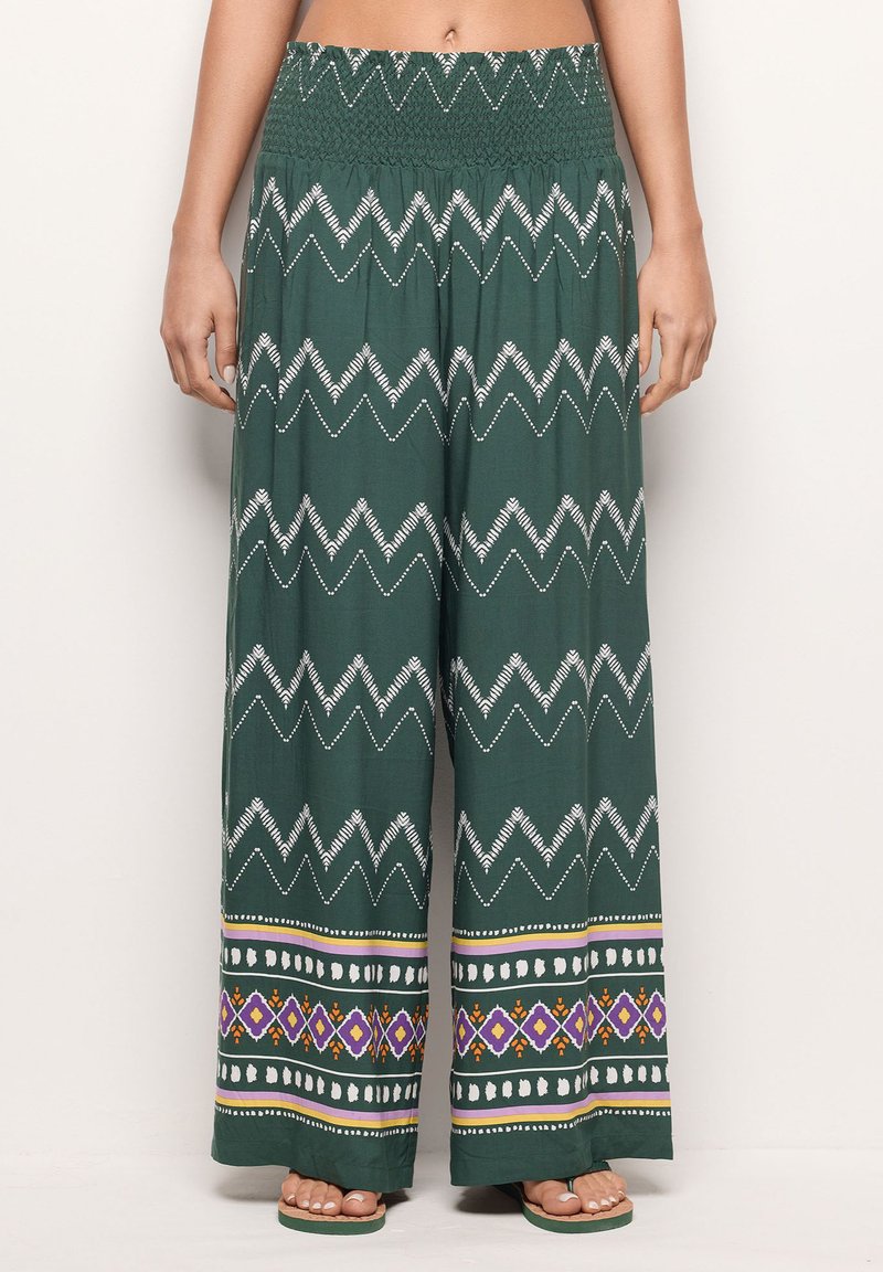 Green wide-leg pants with a smocked waistband. Features white zigzag and patterned hem with purple, yellow, and red accents. Lightweight fabric.