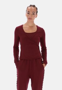 Bourgondische lange mouw wikkel top met een vierkante halslijn, gelaagd ontwerp en gladde stof. Gecombineerd met bijpassende broek met getande zijdetails.