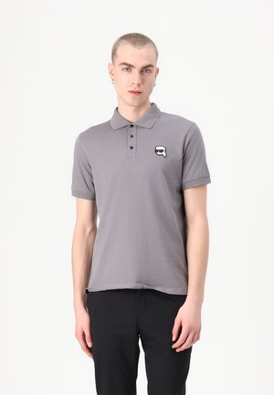 Grå polo skjorte laget av bomull, med krage og tre knapper. Inkluderer et lite, hvitt emblem på venstre bryst. Strukturert stoff.