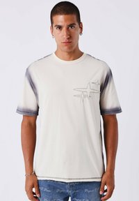 T-shirt in cotone beige chiaro con scollo rotondo, maniche corte e orlo sfumato. Design ricamato sul petto.