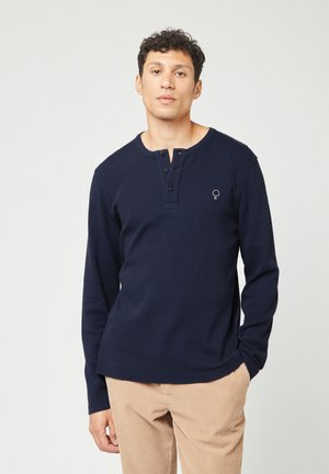Marineblauw langemouw henley-shirt van textuurstof met een knoopsluiting met drie knopen en een geborduurd boompictogram op de linkerborst.