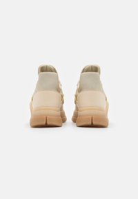 Beige sneakers med en slät yta, vadderad meshrygg och subtila guldaccenter. Sulan är texturerad med ett gummifärgat gummimönster.