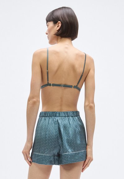 Hátsó nézet egy ujjatlan szatén melltartóról és hozzáillő kék mintás rövidnadrágról, gumis derékrésszel és arany színű kiegészítőkkel.
