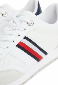 Sneaker athletic bianche con tomaia in mesh traspirante, dettagli in tessuto testurizzato e strisce orizzontali in rosso, bianco e blu navy. Occhielli argentati.