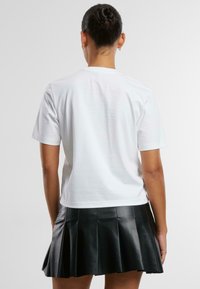 Tricou alb din bumbac cu mâneci scurte, asortat cu o fustă plisată din piele sintetică neagră, evidențiind linii curate și o textură netedă.